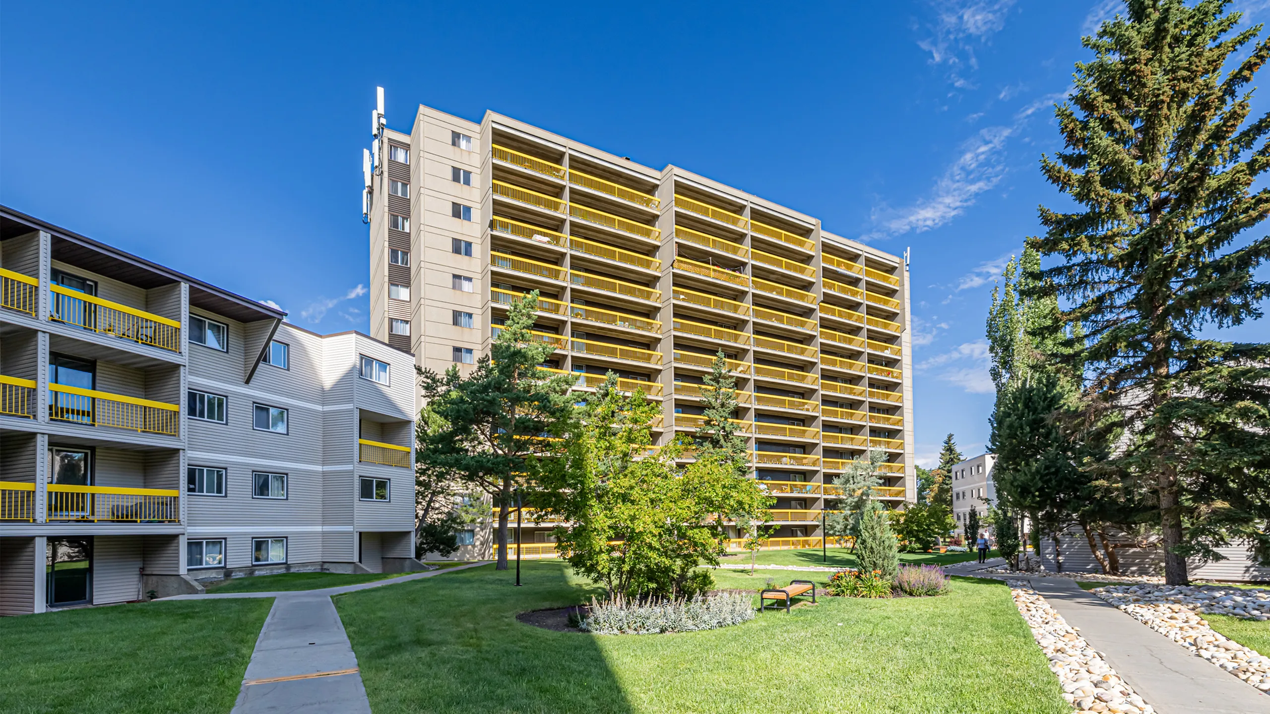 Vibrant urban apartment complex with striking yellow balconies, lush greenery, and clear blue skies.
