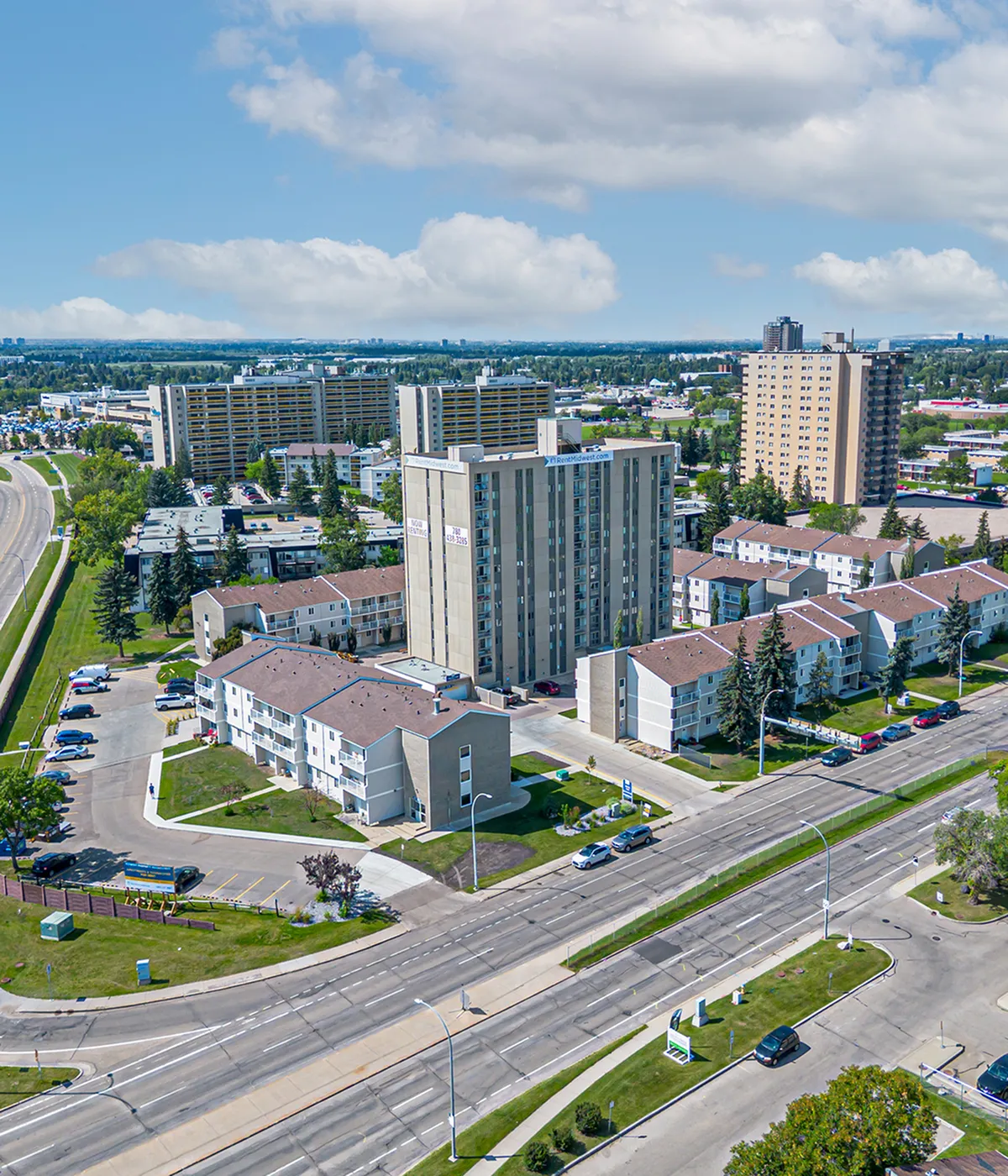 Vibrant aerial view of modern apartment complex with green spaces and convenient access to main roads, offering urban living in a scenic neighborhood.