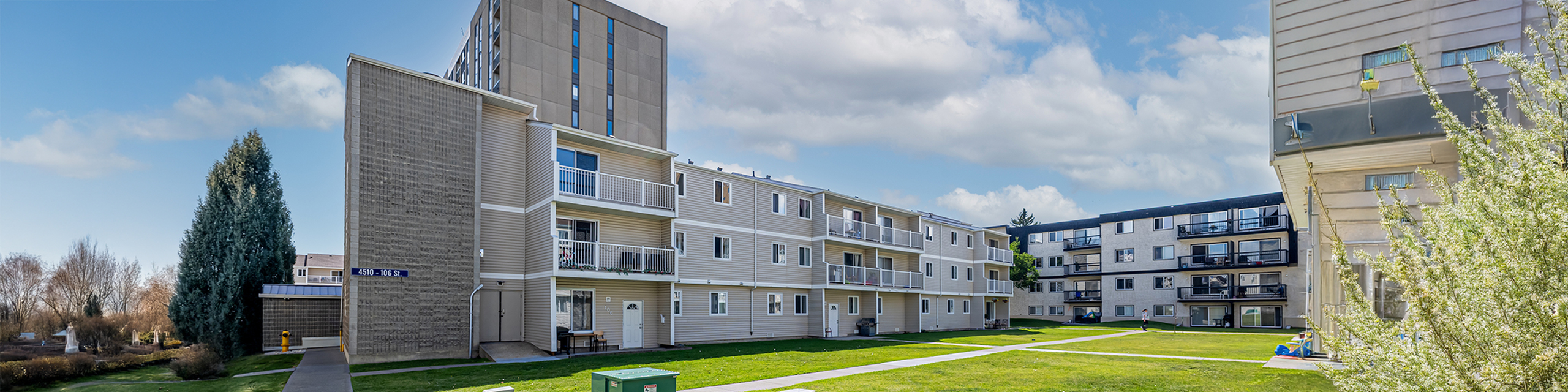 Charming apartment complex with modern architecture, private balconies, and lush green surroundings under a bright, blue sky.