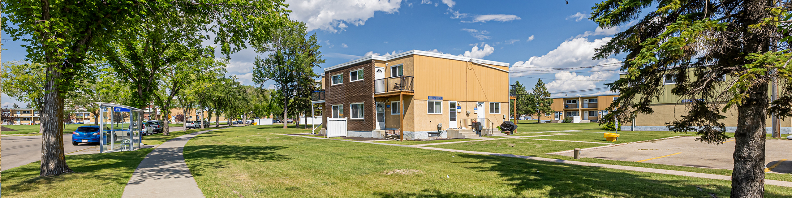 Charming two-story apartment building with spacious grassy surroundings, set in a serene neighborhood under a bright blue sky.