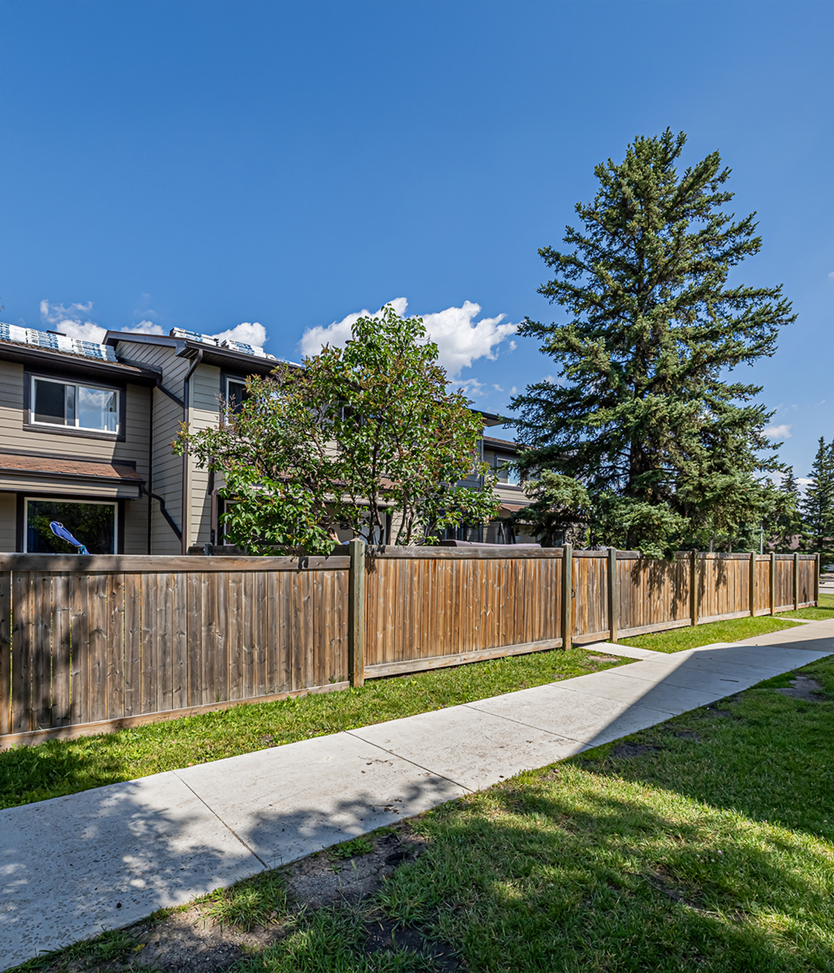 Charming townhouse exterior with wooden fencing and lush greenery under a clear blue sky.