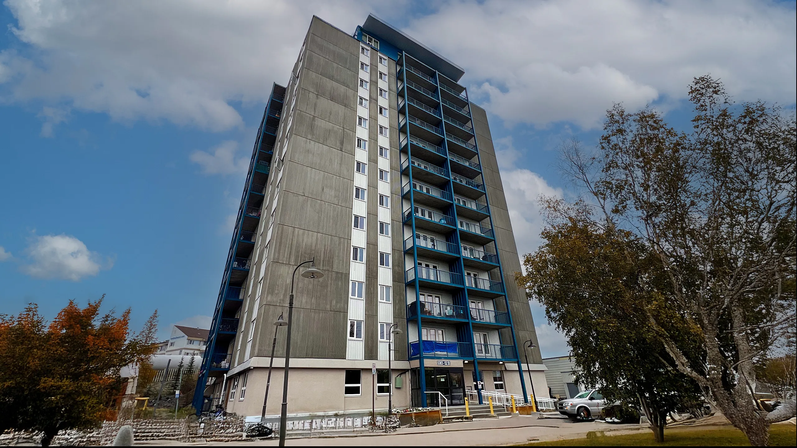 Modern high-rise building with sleek architecture, featuring spacious balconies and surrounded by lush greenery under a vibrant blue sky.
