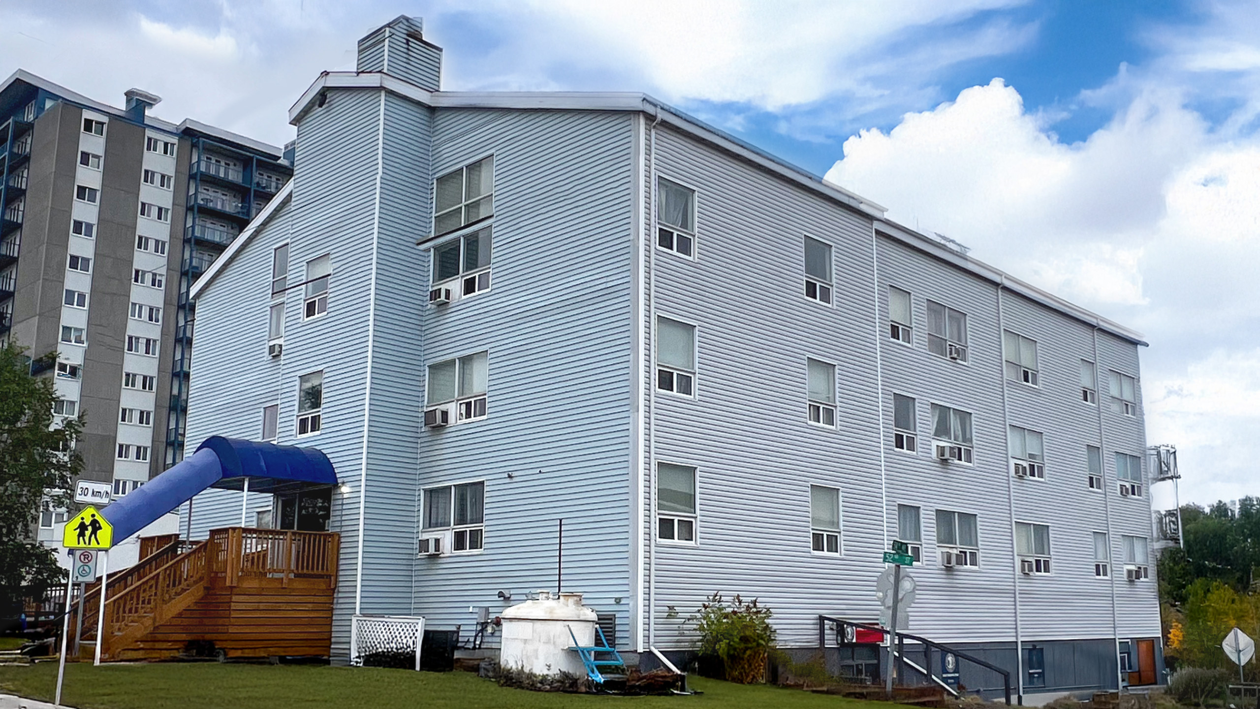 Charming apartment building with contemporary blue siding, featuring multiple windows and a welcoming entrance, set against a backdrop of blue skies.