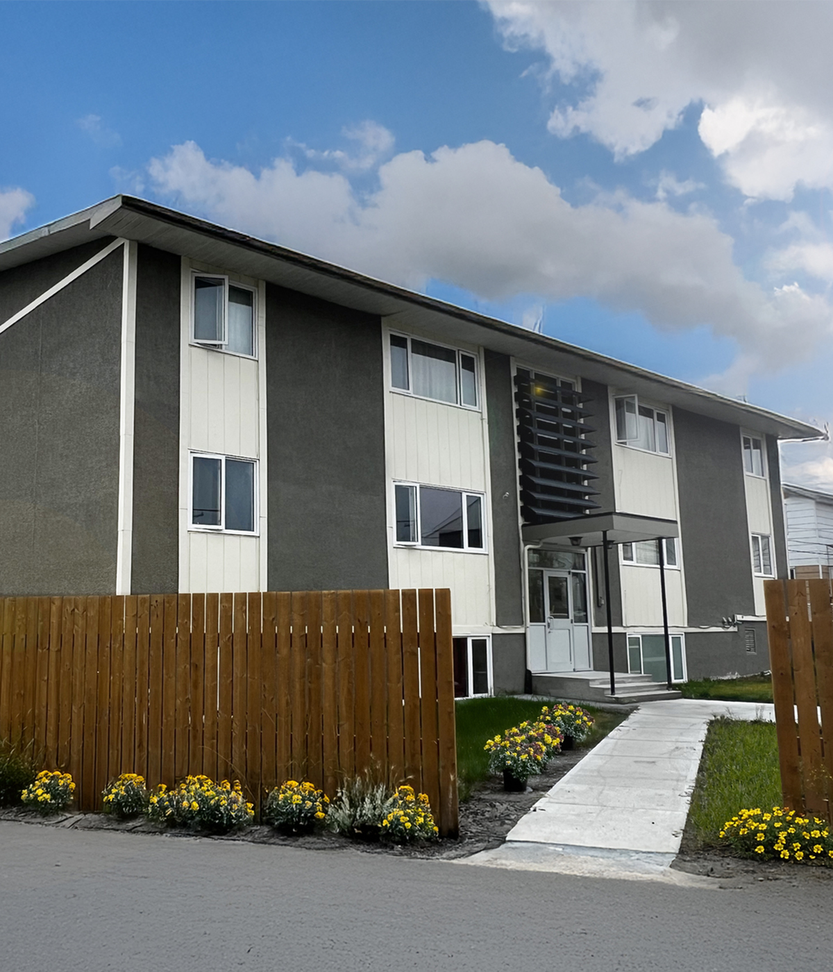 Modern apartment building with clean lines, lush landscaping, and inviting walkway under a bright blue sky.