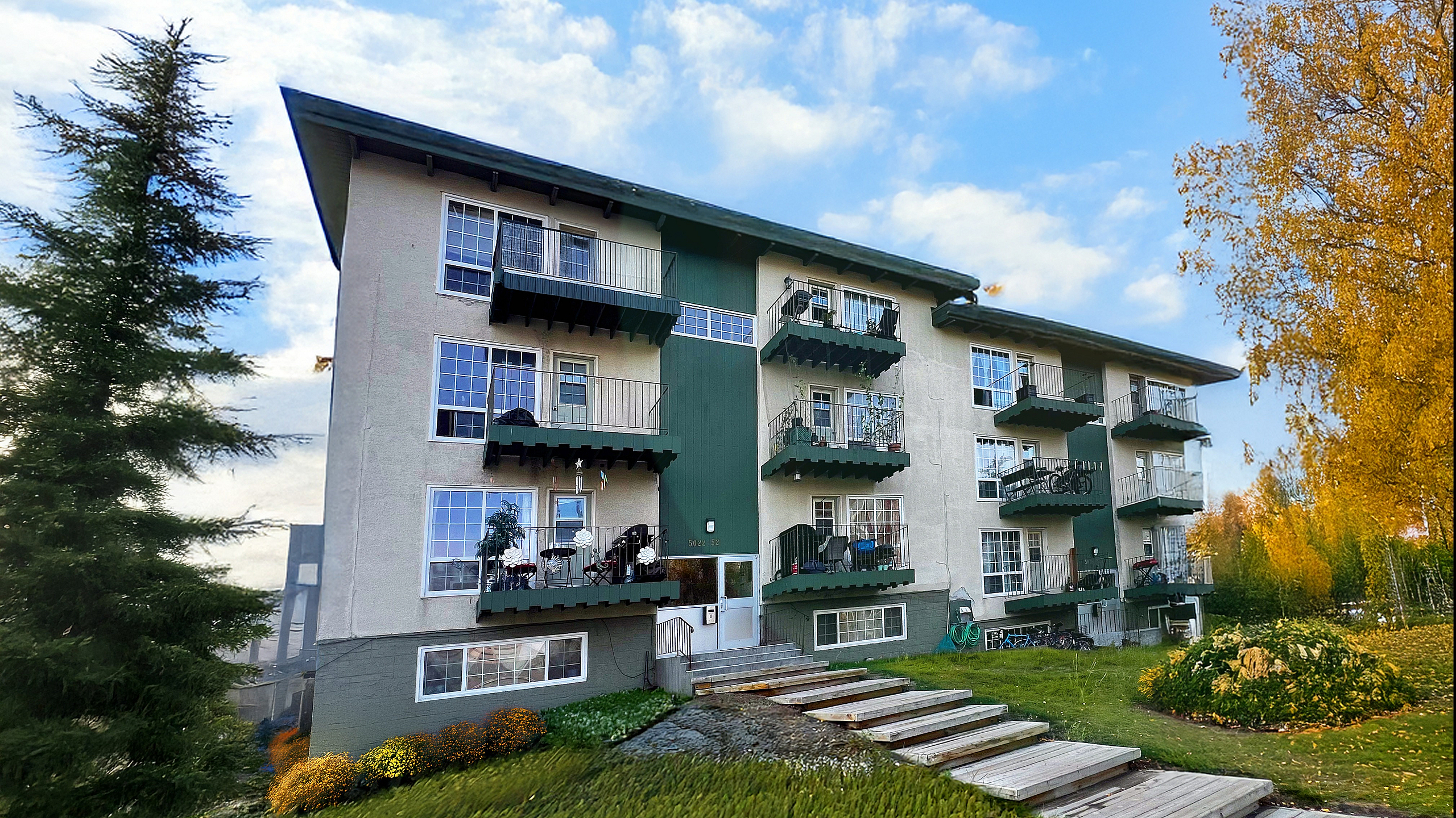 Charming apartment building with balconies, set amidst lush greenery and vibrant autumn foliage, offering serene and picturesque views.