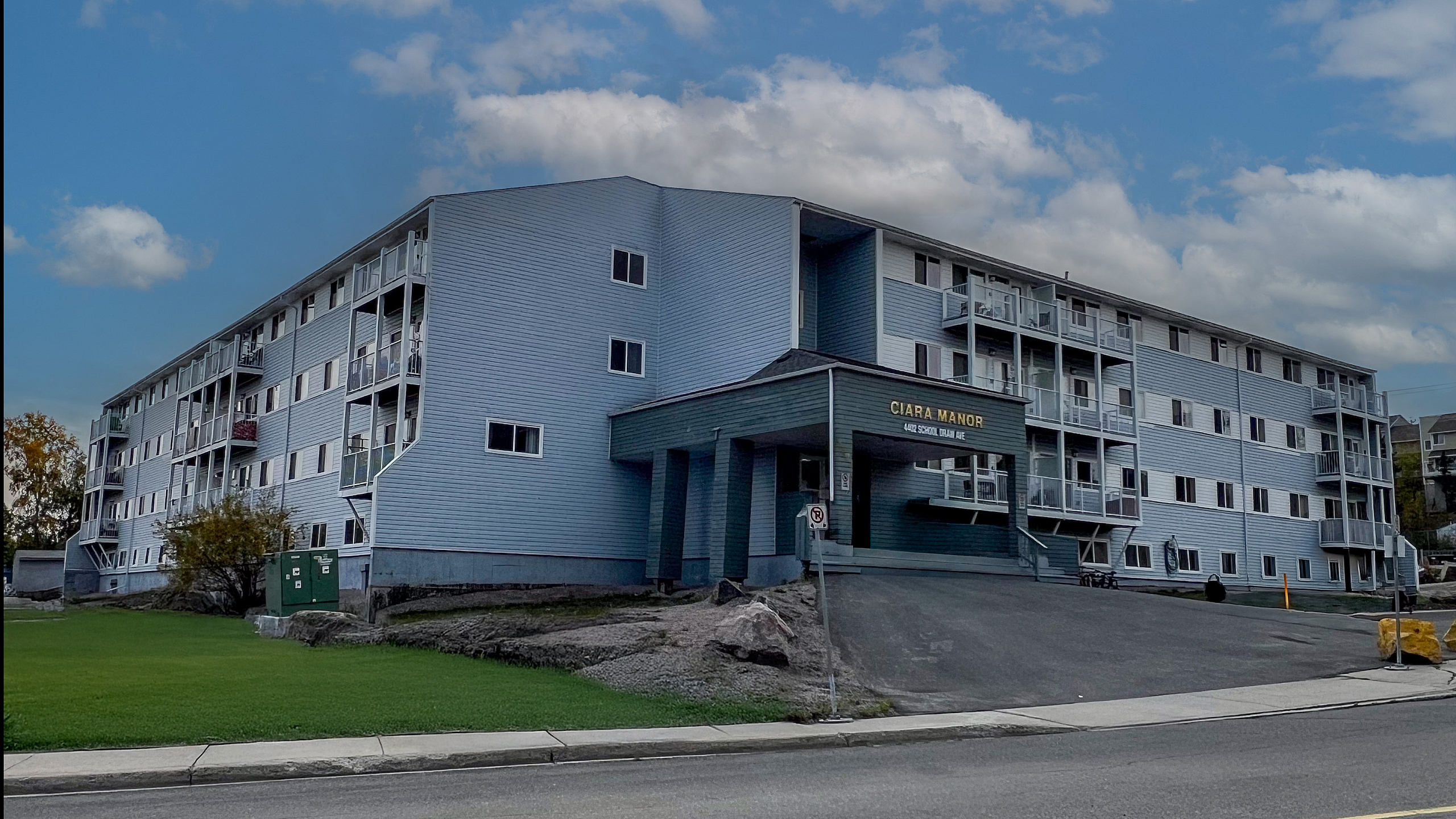 Charming four-story apartment building with modern balconies set against a vibrant blue sky, offering comfortable living spaces on a peaceful street.
