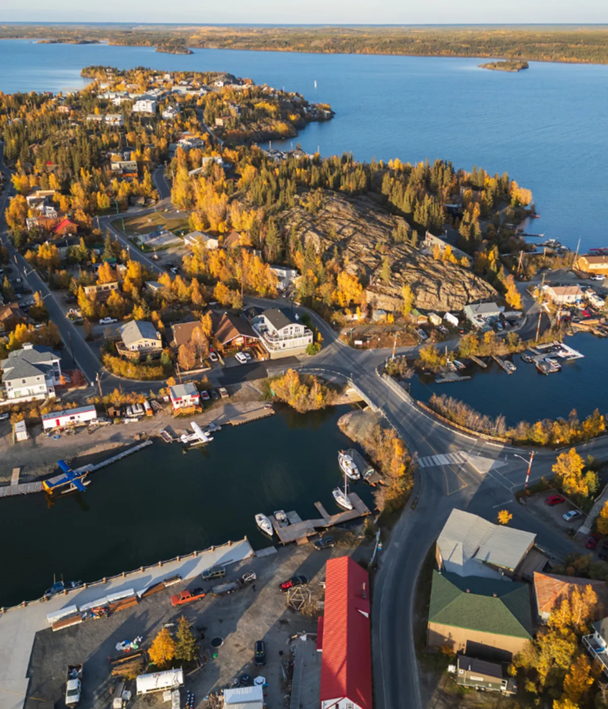 Stunning aerial view of a scenic lakeside community bathed in golden autumn colors, featuring waterfront homes, a vibrant marina, and lush landscapes.