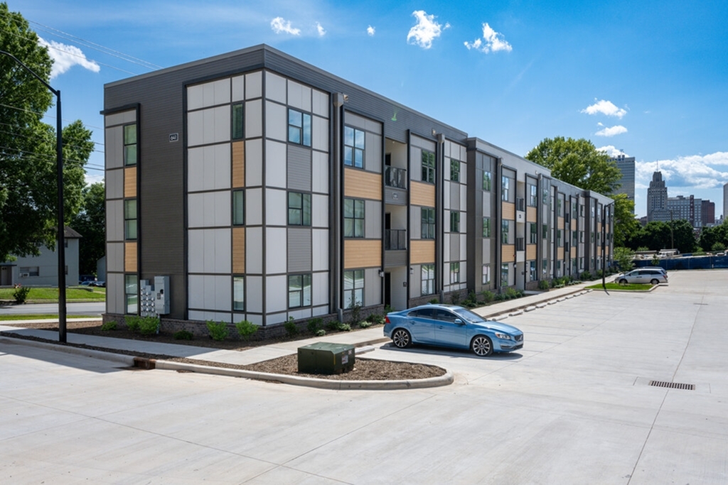 Modern apartment building with sleek, contemporary design and vibrant city skyline in the background, bathed in sunlight.