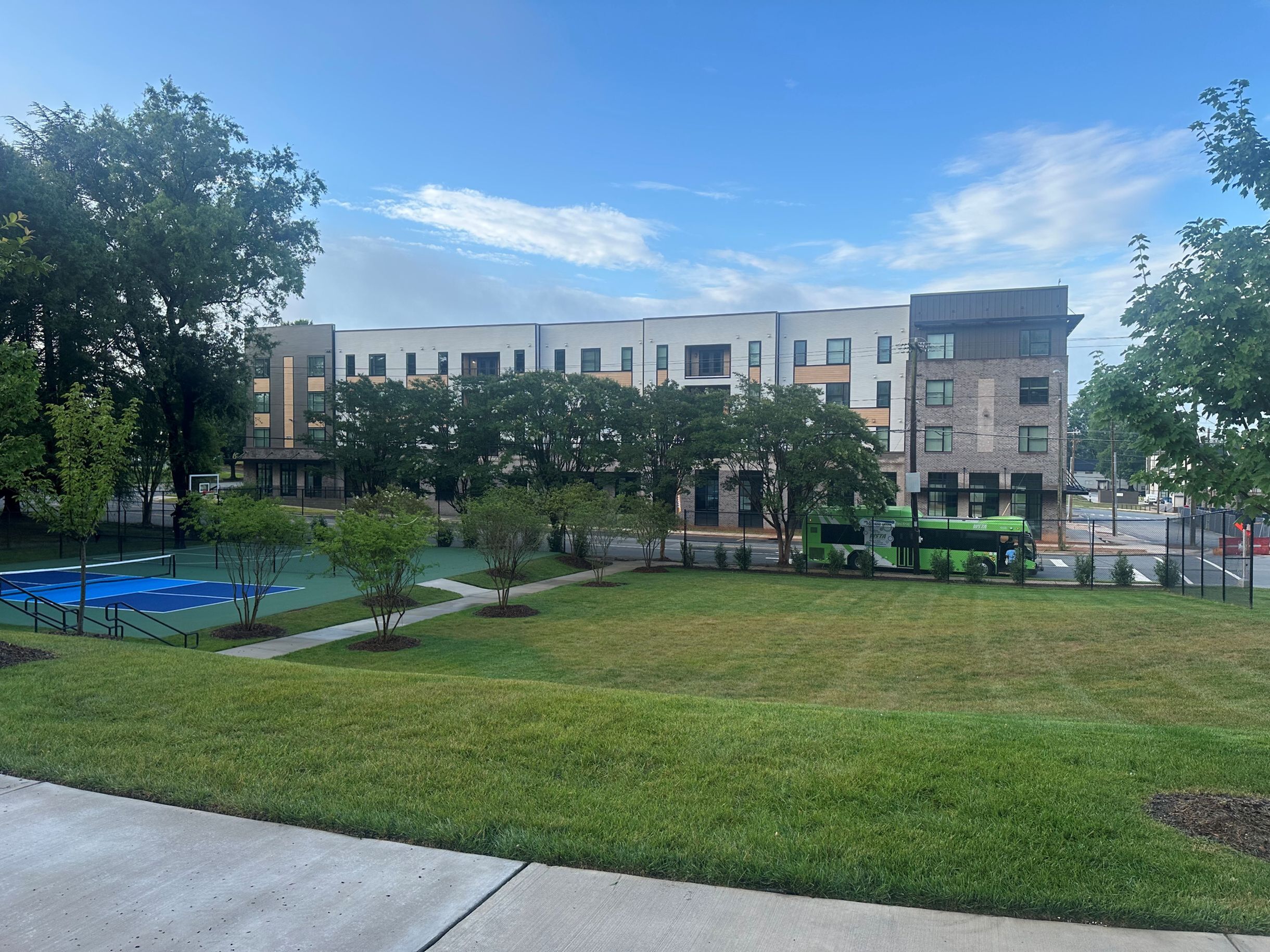 Modern apartment building with lush green lawns, a vibrant basketball court, and convenient public transport links in a serene community setting.