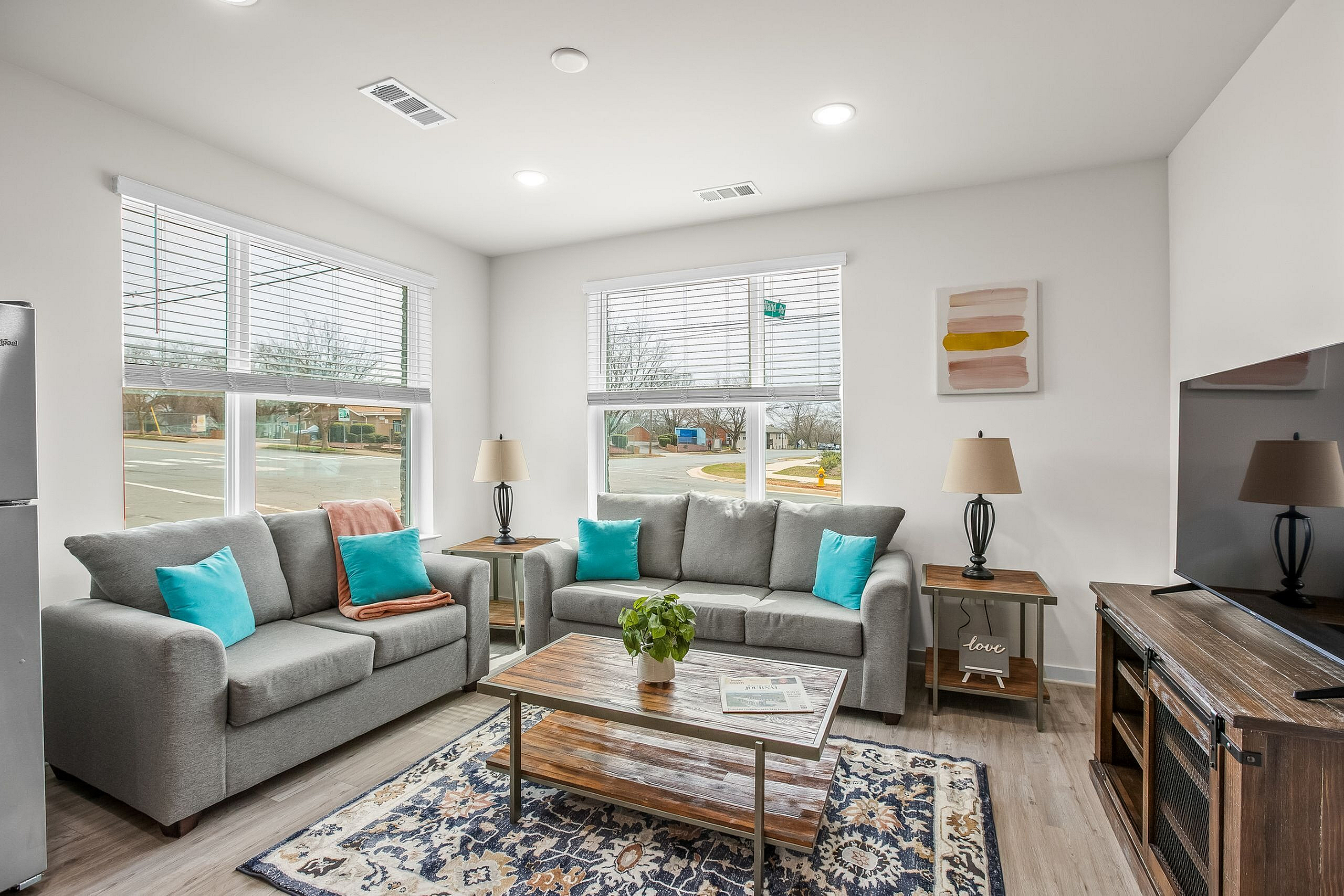 Bright and inviting living room with contemporary gray sofas, vibrant teal cushions, and large windows filling the space with natural light.