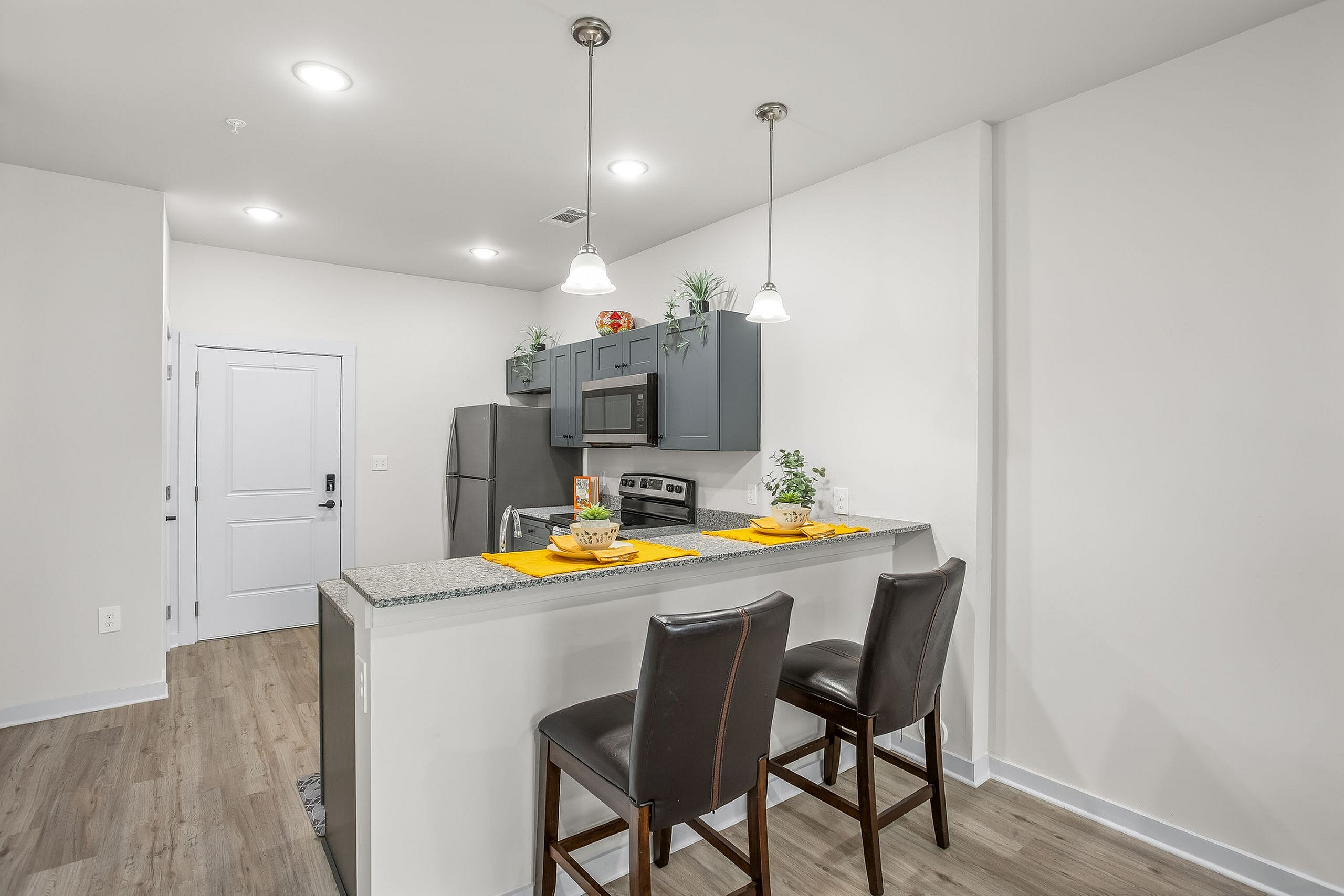 Modern kitchen with elegant pendant lighting, granite countertops, and bar seating in a contemporary apartment.