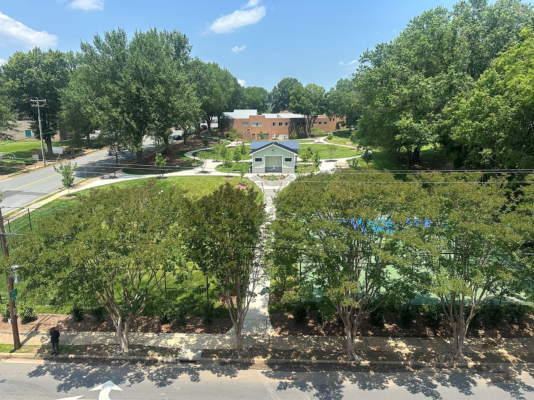 Vibrant community park scene with lush greenery, walking paths, and a charming pavilion under a clear blue sky.