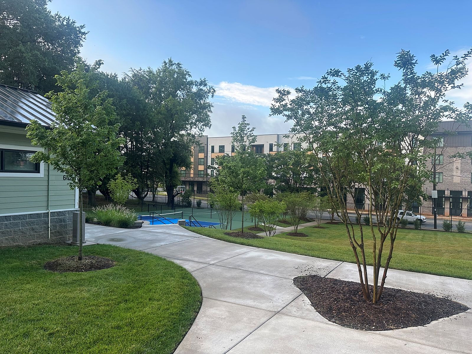 Charming apartment complex with lush greenery, modern architecture, and a nearby basketball court for active living.