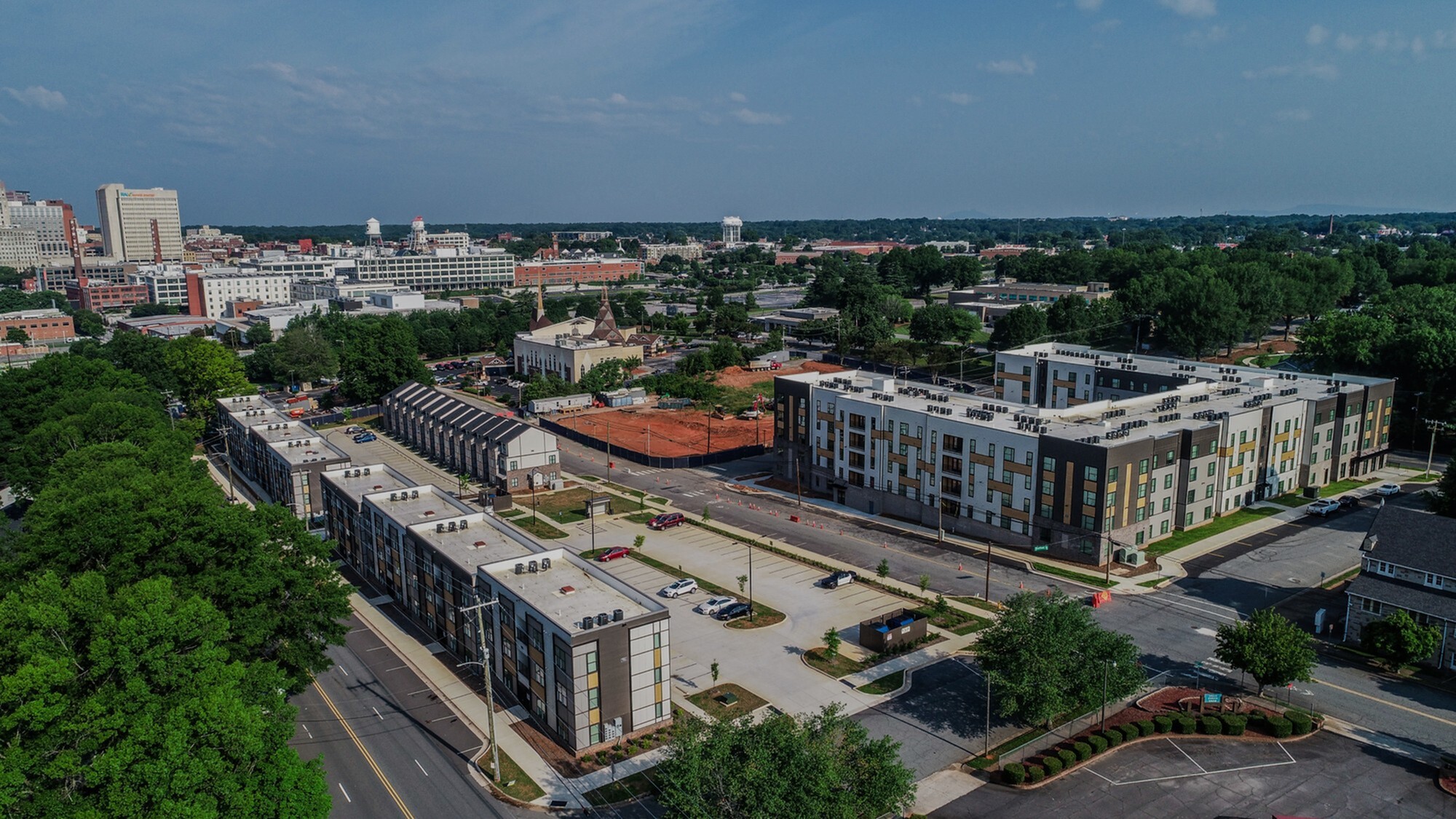 Aerial view of modern apartment complex surrounded by greenery and cityscape, showcasing convenient urban living in a picturesque setting.