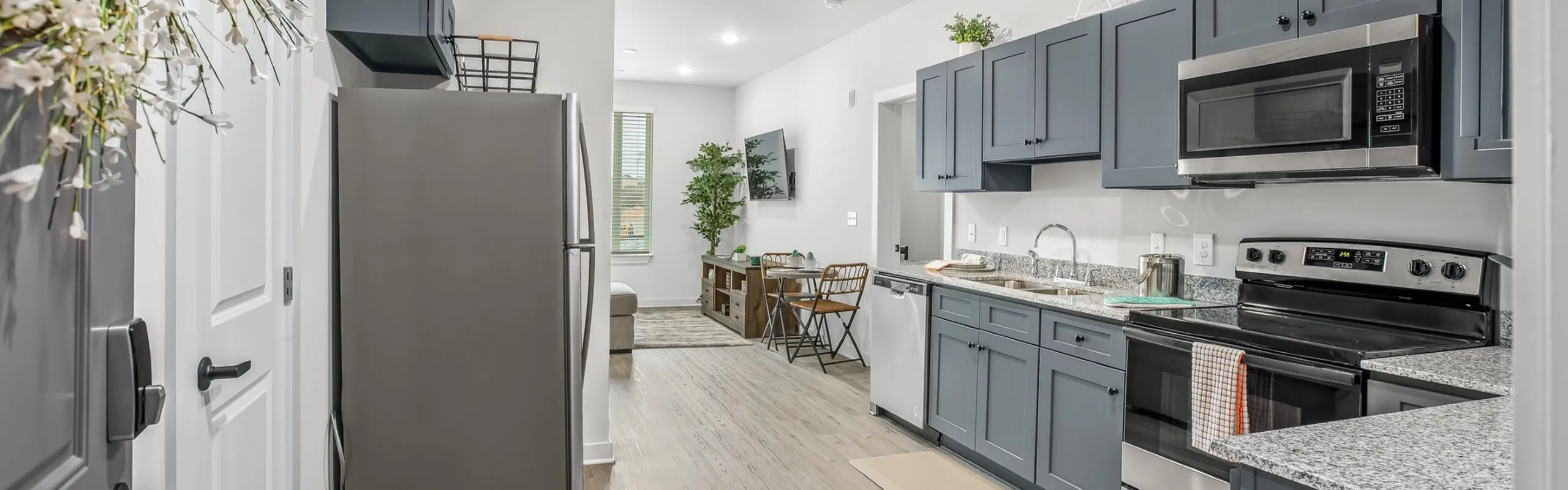 Modern kitchen with sleek grey cabinets, granite countertops, and stainless steel appliances leading to a cozy, well-lit living area.