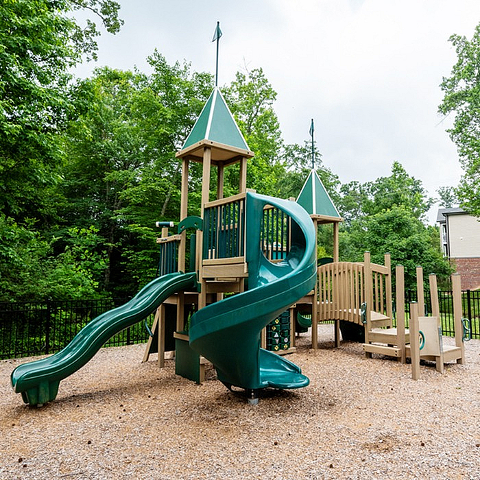 Captivating playground with green slides and wooden structures surrounded by lush trees.