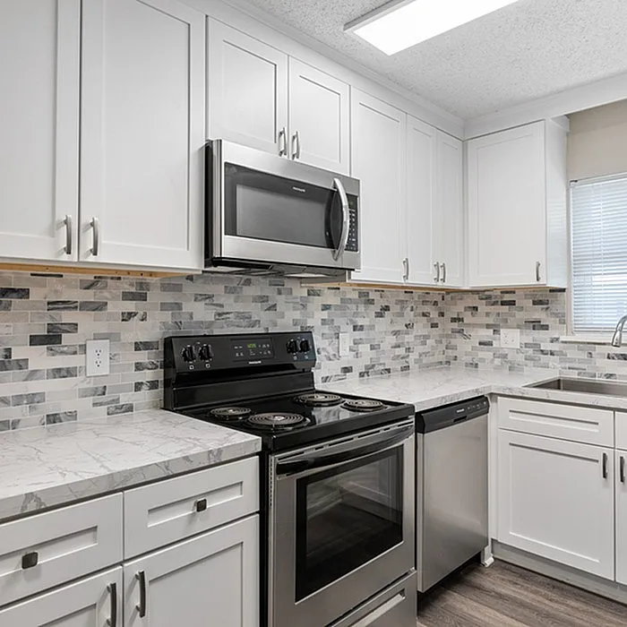 Contemporary kitchen featuring sleek white cabinets, marble countertops, stainless steel appliances, and a tiled backsplash.