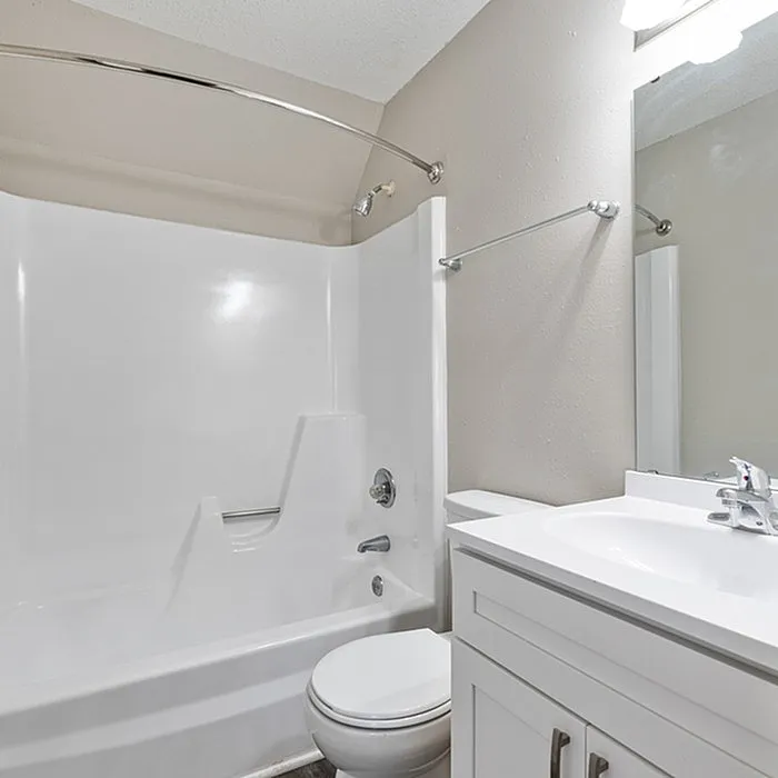 Bright and modern bathroom featuring a sleek white bathtub, toilet, and vanity with a mirror.