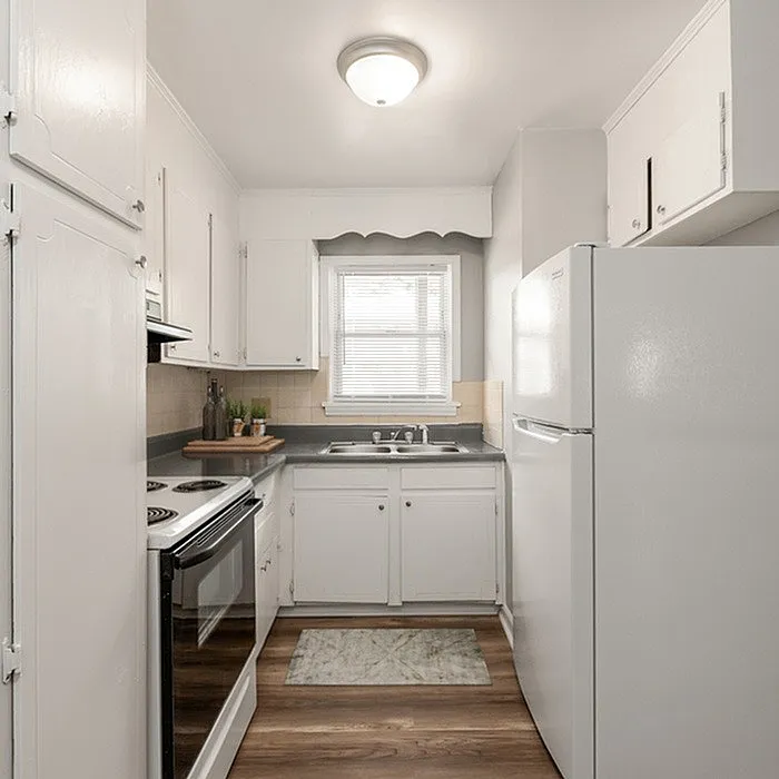 Bright, compact kitchen with white cabinets, modern appliances, and natural light from a window.