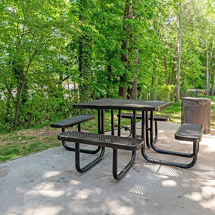 Serene outdoor seating area with a metal picnic table surrounded by lush green trees.