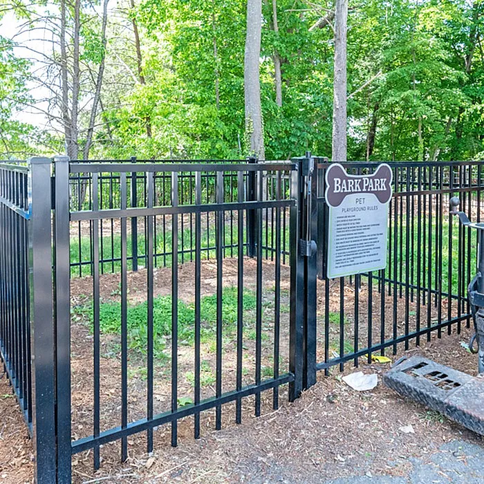 Inviting fenced dog park surrounded by lush green trees and a welcoming entrance sign.
