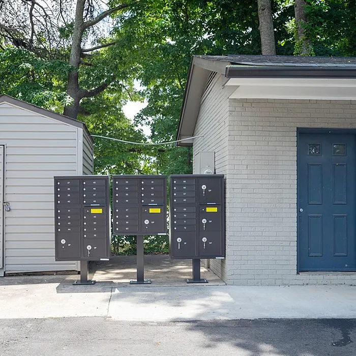 Outdoor mailboxes by an apartment building amidst a lush green backdrop.