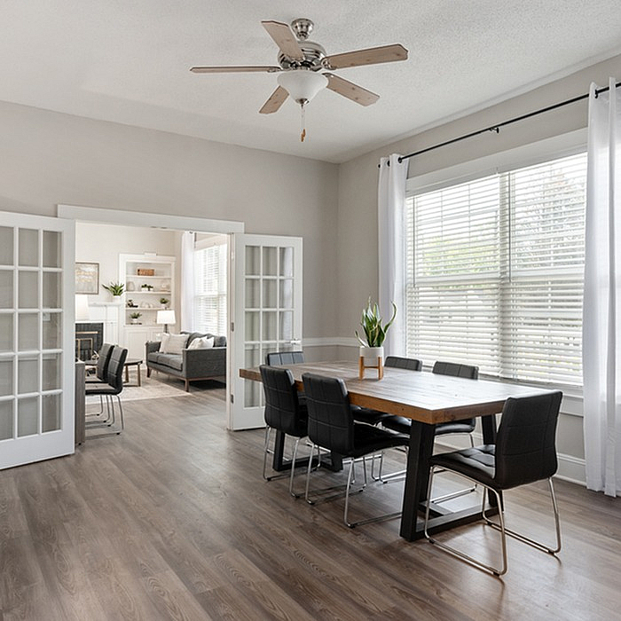 Bright dining area with modern table, stylish chairs, and glass doors leading to a cozy living room.