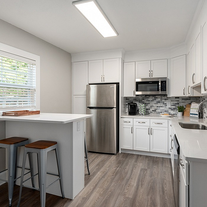 Bright and modern kitchen with white cabinets, stainless steel appliances, and wood flooring.