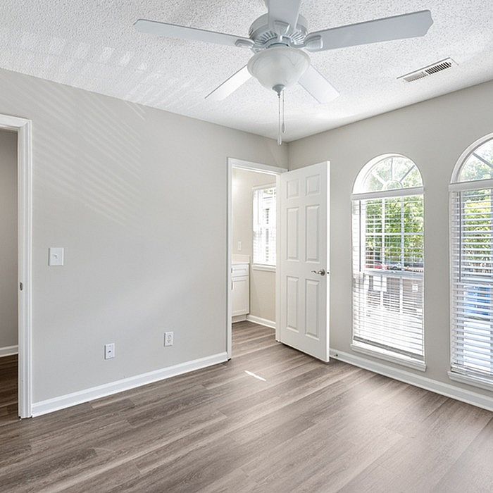 Bright and inviting room with elegant wooden flooring and large arched windows, featuring a modern ceiling fan and ample natural light.