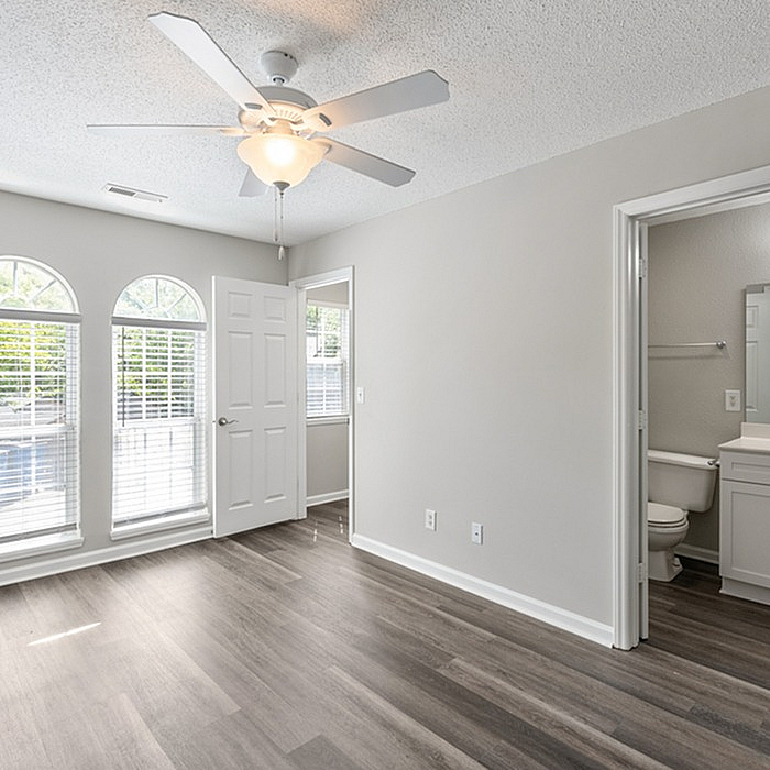 Bright bedroom with large windows, sleek ceiling fan, and modern flooring, adjacent to a stylish ensuite bathroom.
