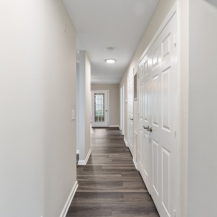 Bright and inviting hallway with sleek wooden flooring, contemporary doors, and modern lighting, leading to a glass-paneled exit.