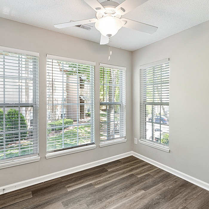 Bright room with large windows, wood flooring, and ceiling fan in a serene residential setting.
