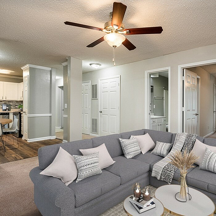 Elegant open-concept living space featuring a cozy L-shaped sofa, stylish ceiling fan, and modern kitchen in the background.
