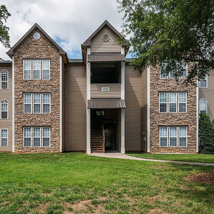Charming apartment exterior featuring elegant stone facade, lush green surroundings, and inviting entrance with classic architectural design.