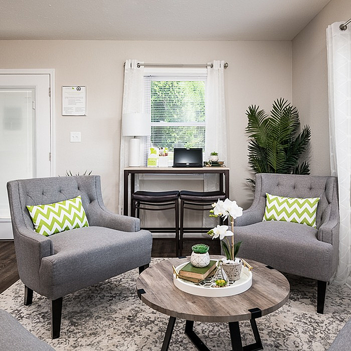 Chic living room with modern gray armchairs, vibrant green accents, a stylish coffee table, and a cozy workspace by a sunlit window.