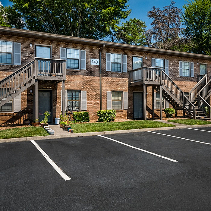Charming brick apartment building with individual entrances, surrounded by lush greenery and spacious parking facilities.