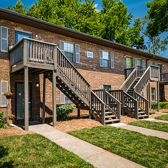 Charming brick apartment complex with private balcony access, surrounded by lush greenery and inviting walkways.