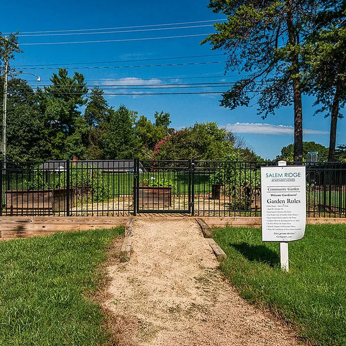 Welcoming entrance to a community garden with lush greenery and a charming pathway, perfect for relaxing and enjoying nature.