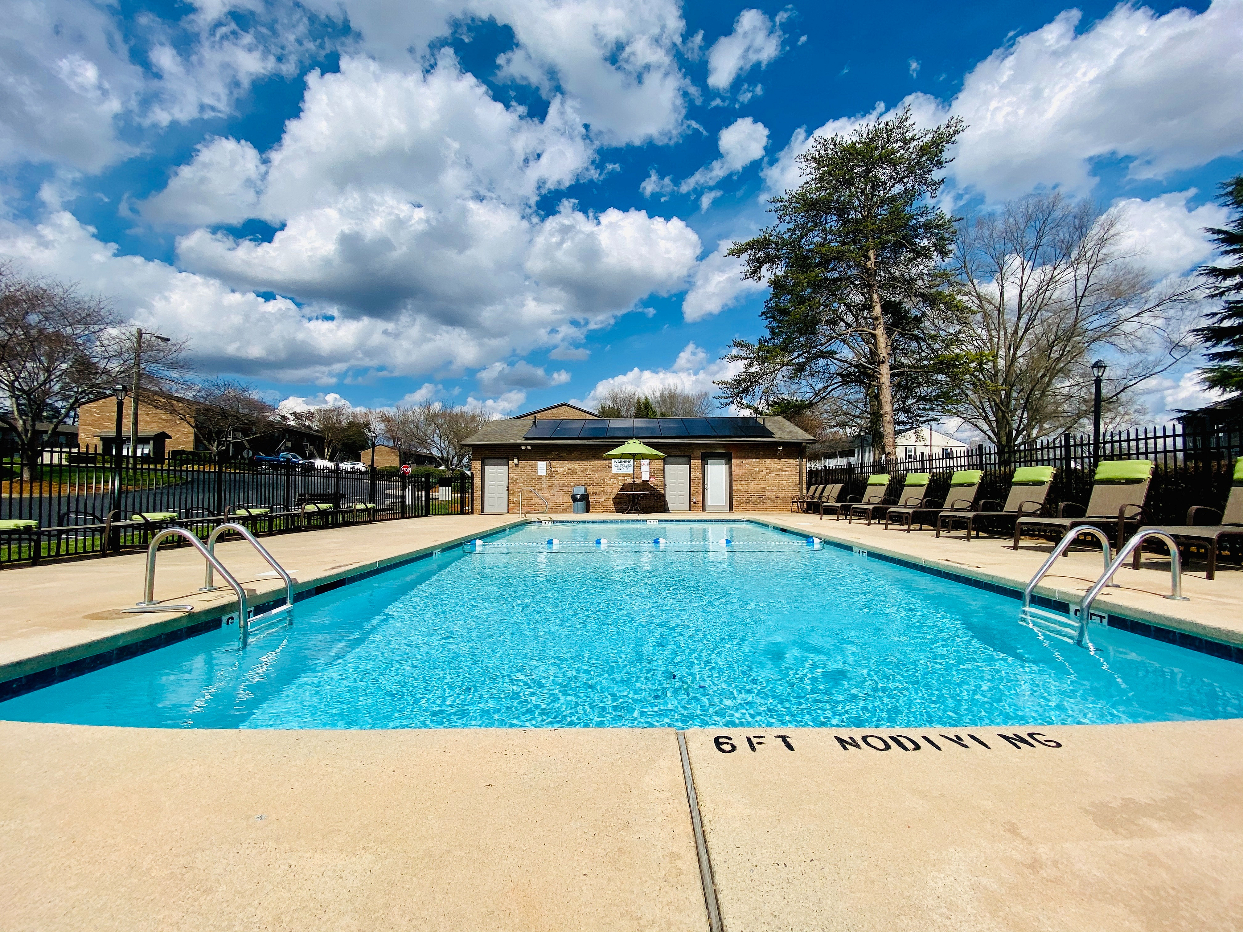 Inviting outdoor swimming pool with sun loungers, surrounded by lush greenery and blue skies, perfect for relaxation.