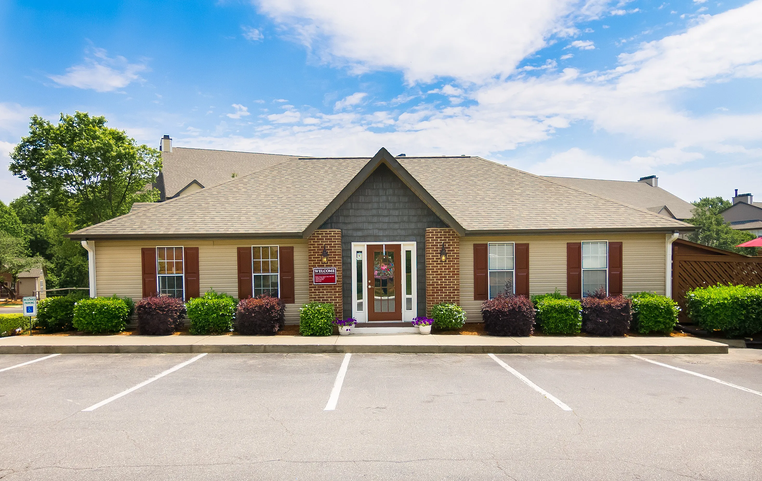 Charming single-story apartment with elegant brick facade, lush landscaping, and welcoming entrance under a bright blue sky.