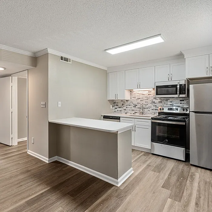 Modern open kitchen with sleek stainless steel appliances, stylish backsplash, and elegant cabinetry, complemented by warm wood flooring.