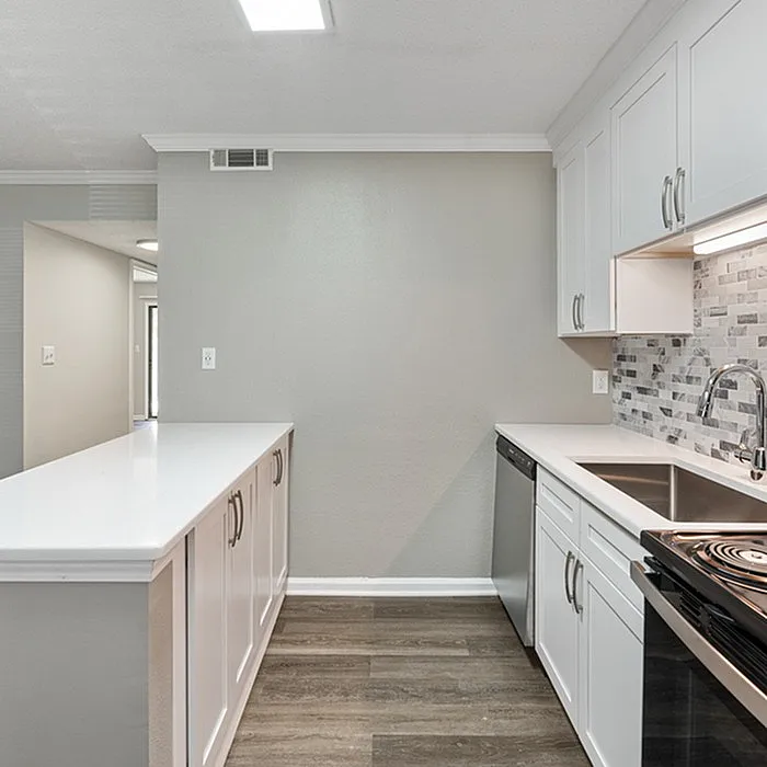 Modern kitchen with sleek white cabinetry, stainless steel appliances, and elegant tile backsplash in a cozy apartment setting.