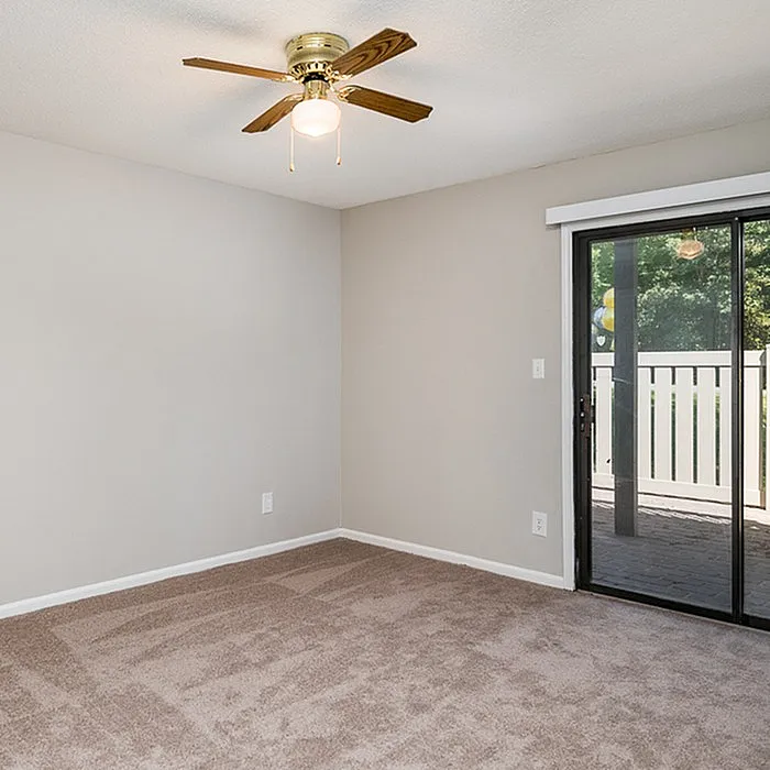 Bright, airy bedroom with plush carpet, ceiling fan, and large glass doors opening to a serene patio.