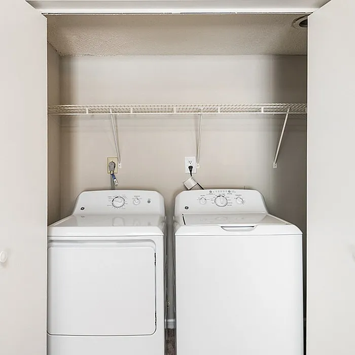 Modern laundry nook featuring sleek washer and dryer with convenient overhead shelving.