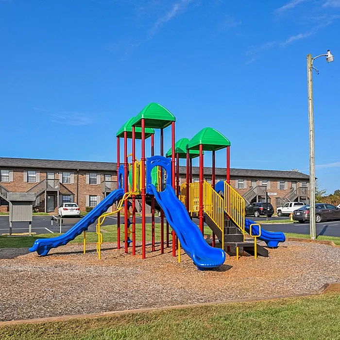 Bright and inviting playground with colorful slides and climbing structures, set in a vibrant community backdrop under a clear blue sky.