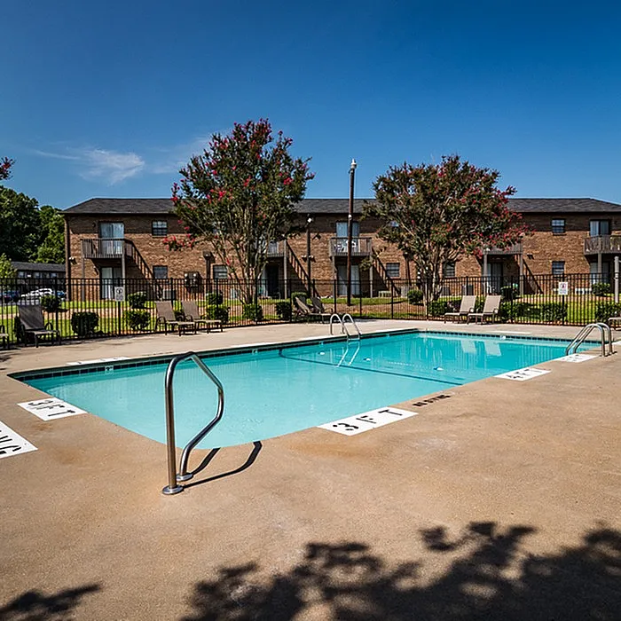 Inviting apartment complex with a refreshing outdoor pool surrounded by lush greenery and elegant lounge chairs.
