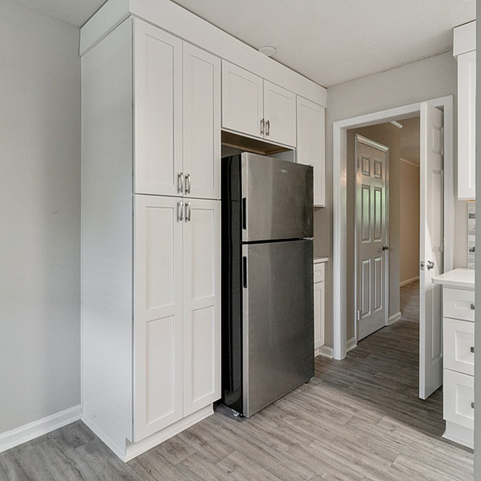 Modern kitchen design with sleek stainless steel refrigerator, elegant white cabinetry, and stylish wood flooring, offering a perfect blend of functionality and aesthetics.
