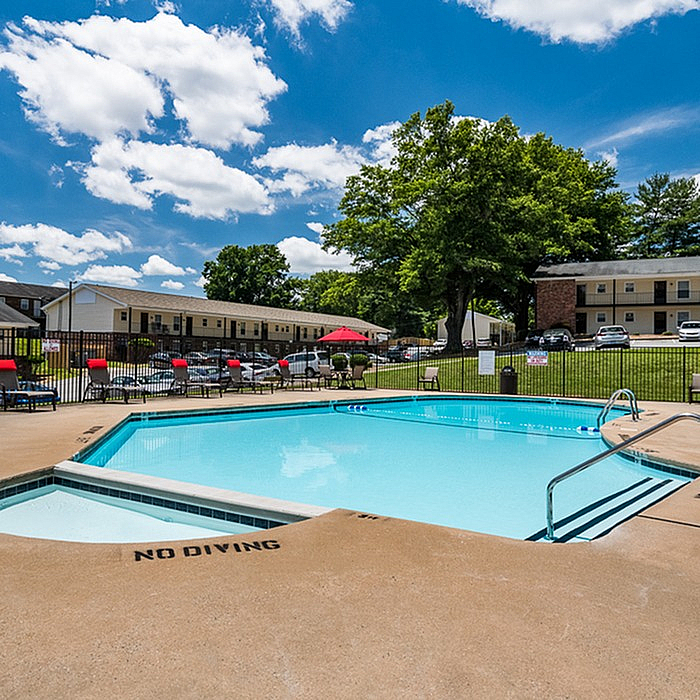 Inviting outdoor pool area with bright red lounge chairs and scenic green surroundings under a vibrant blue sky, offering a perfect relaxation spot.