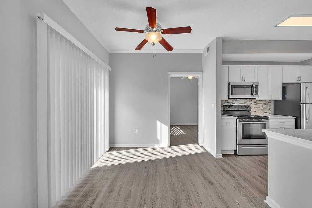 Bright modern apartment featuring sleek gray flooring, stainless steel kitchen appliances, and large sliding glass doors for abundant natural light.