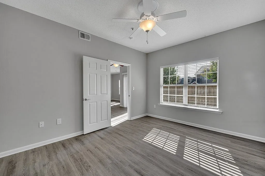Bright and airy bedroom with elegant gray walls, a large window letting in natural light, and stylish wood flooring.